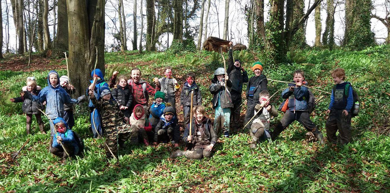 A group of children in muddy wellies and face paint cheering in the woods